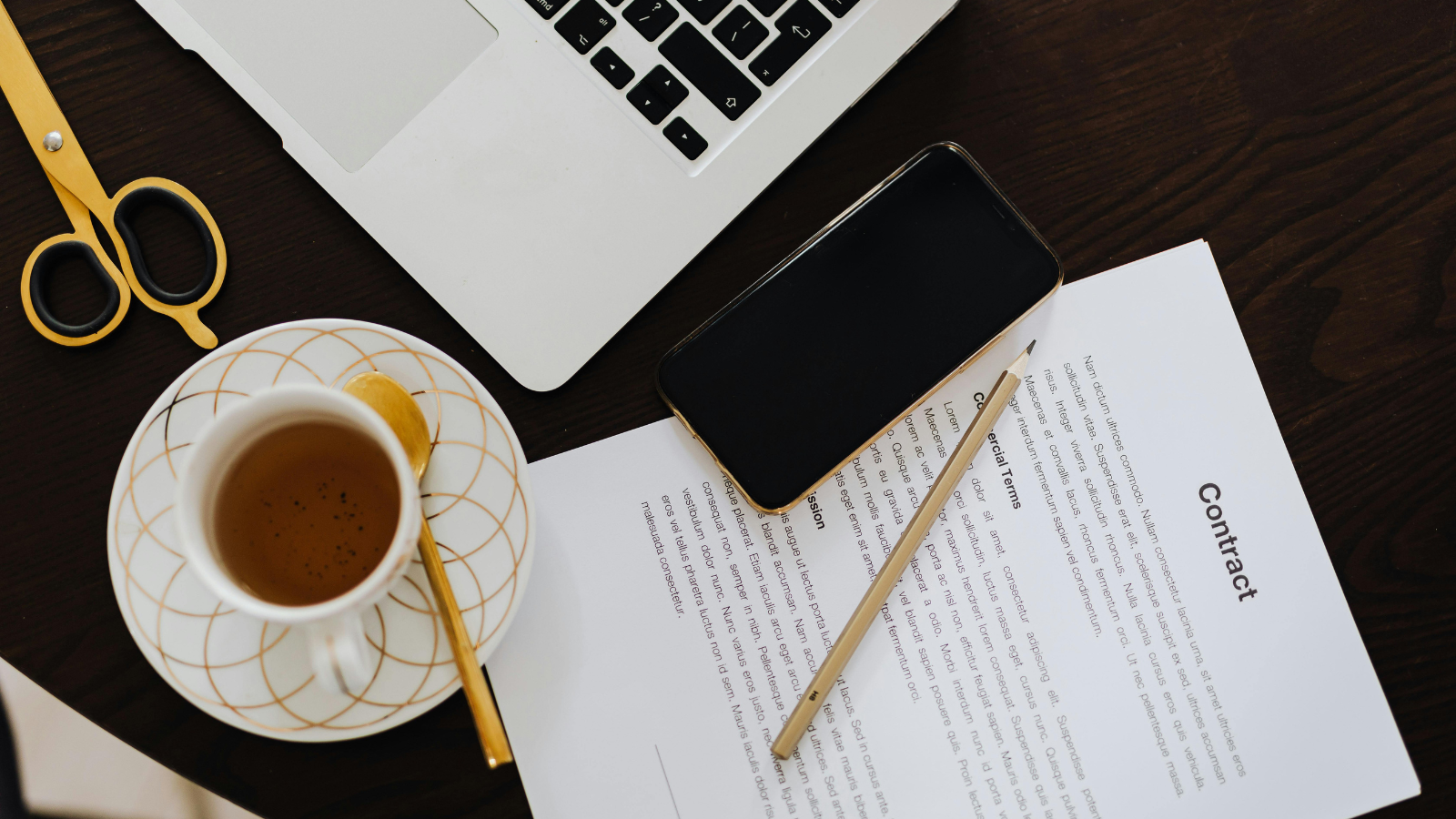A contract next to a coffee cup, mobile phone, laptop, and scissors. 